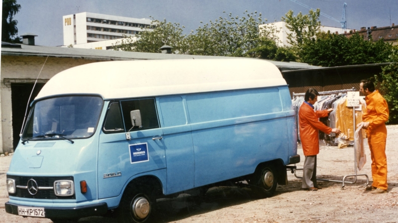 Zwei Hermes Zusteller sortieren Kleidungswaren vor einem blauen Hermes Lieferwagen (Foto: Hermes)