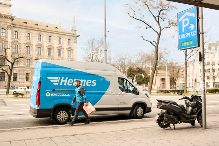 Hermes Zusteller mit E-Transporter bei der Arbeit in München. Hermes-Sendungen kommen in der bayerischen Landeshauptstadt seit März 2026 flächendeckend elektrisch an Haustüren und PaketShops. (Foto: Hermes Germany / Willing-Holtz)

Hermes Germany; E-Mobilität; E-Transporter; Nachhaltigkeit; München; Zustellflotte; Fahrzeugflotte; Letzte Meile; City-Logistik; E-Mobility; Elektrofahrzeuge
